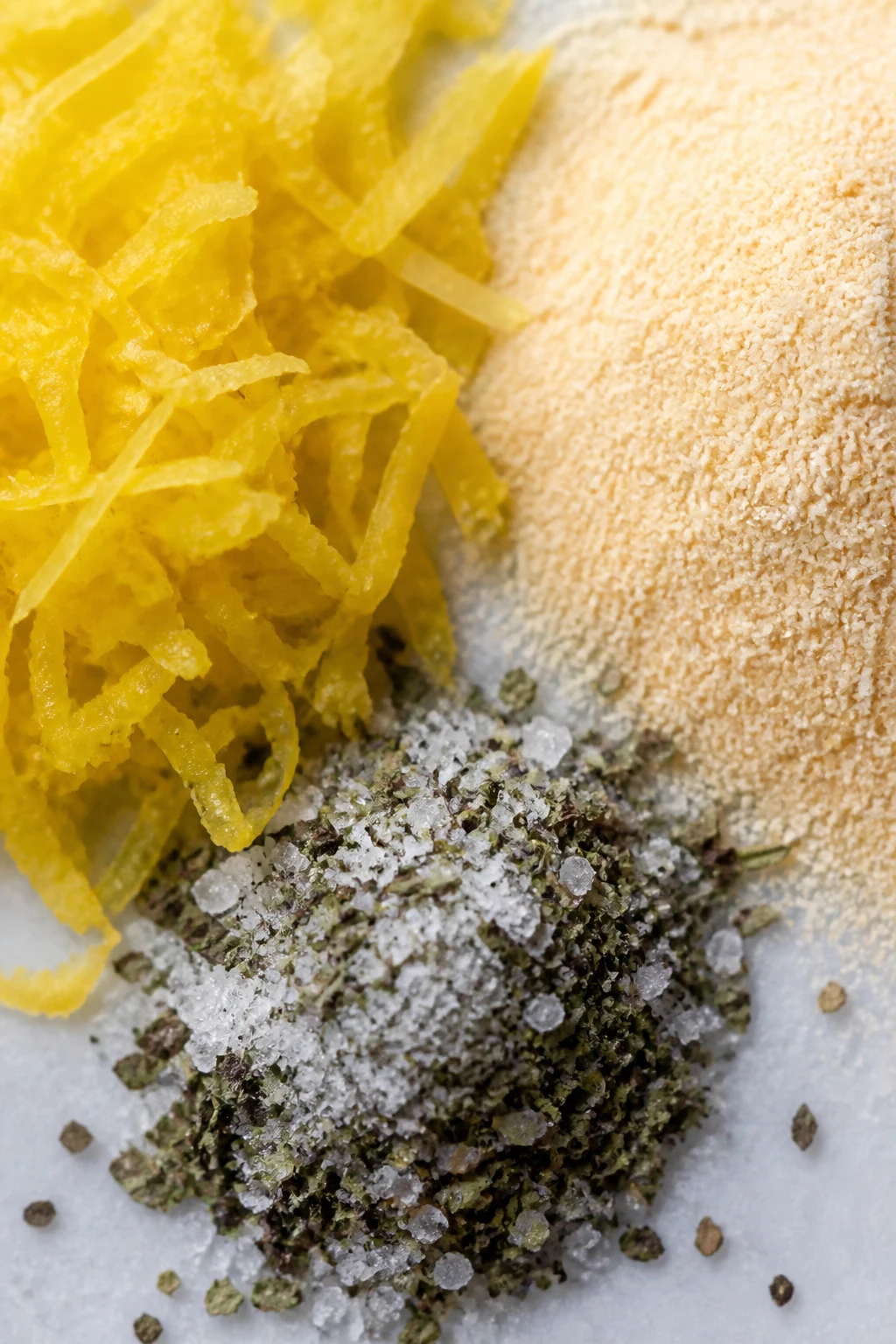 Closeup of lemon zest and garlic powder beside a pinch of basil salt