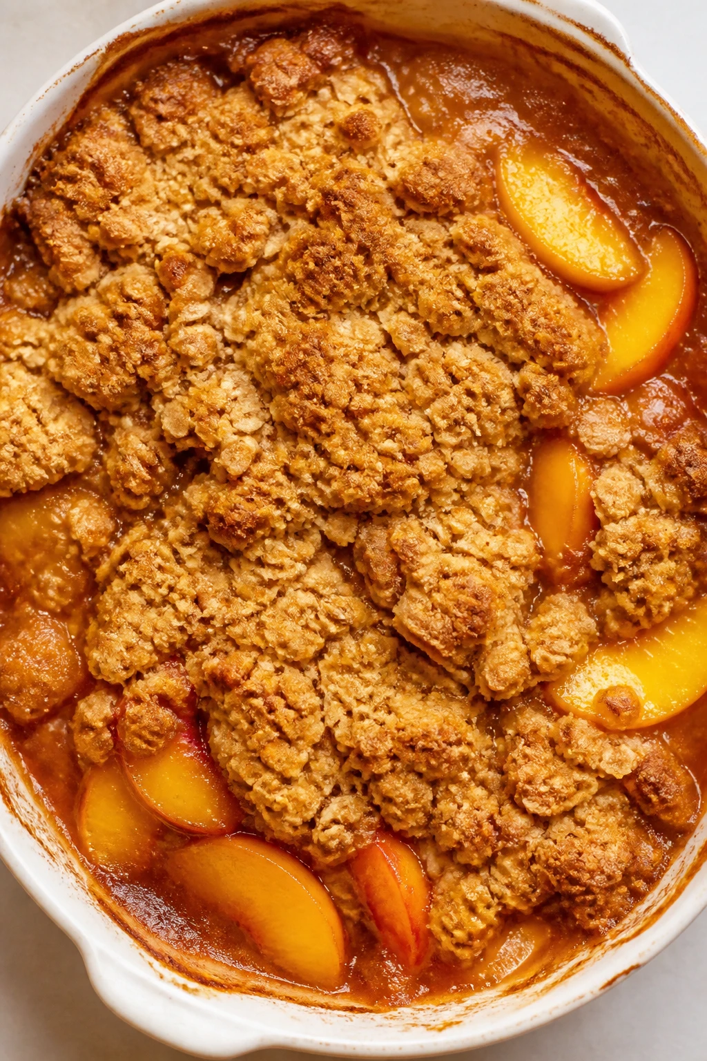 Top-down closeup of golden peach crisp bubbling in dish