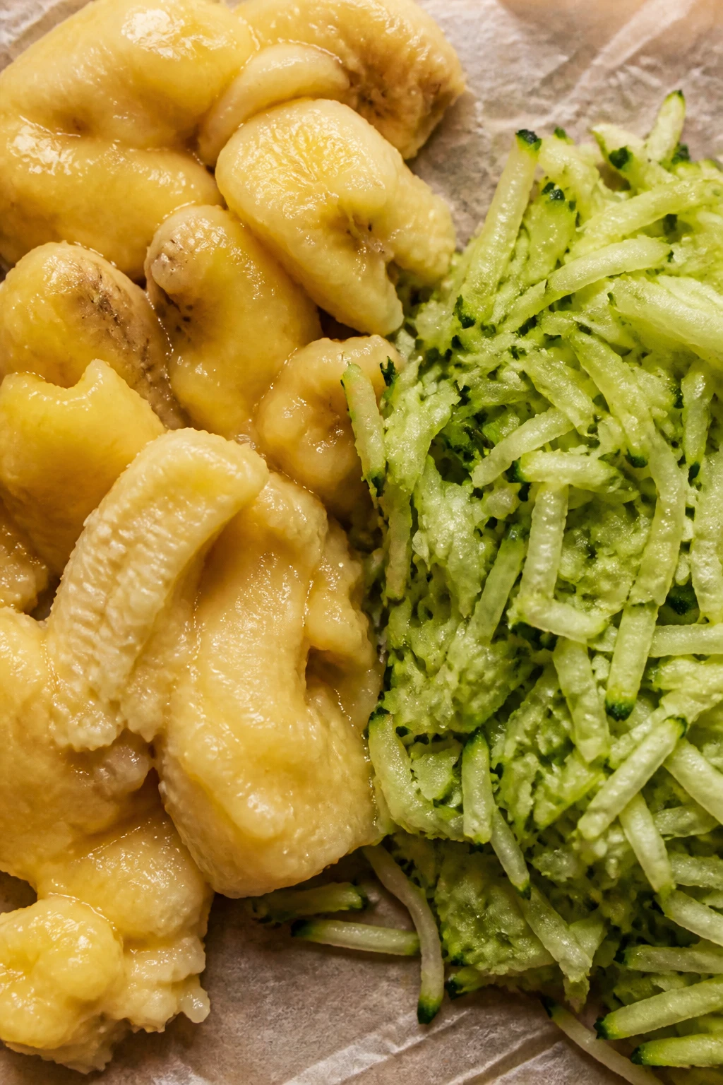 closeup dump of ripe bananas beside zucchini shreds on parchment