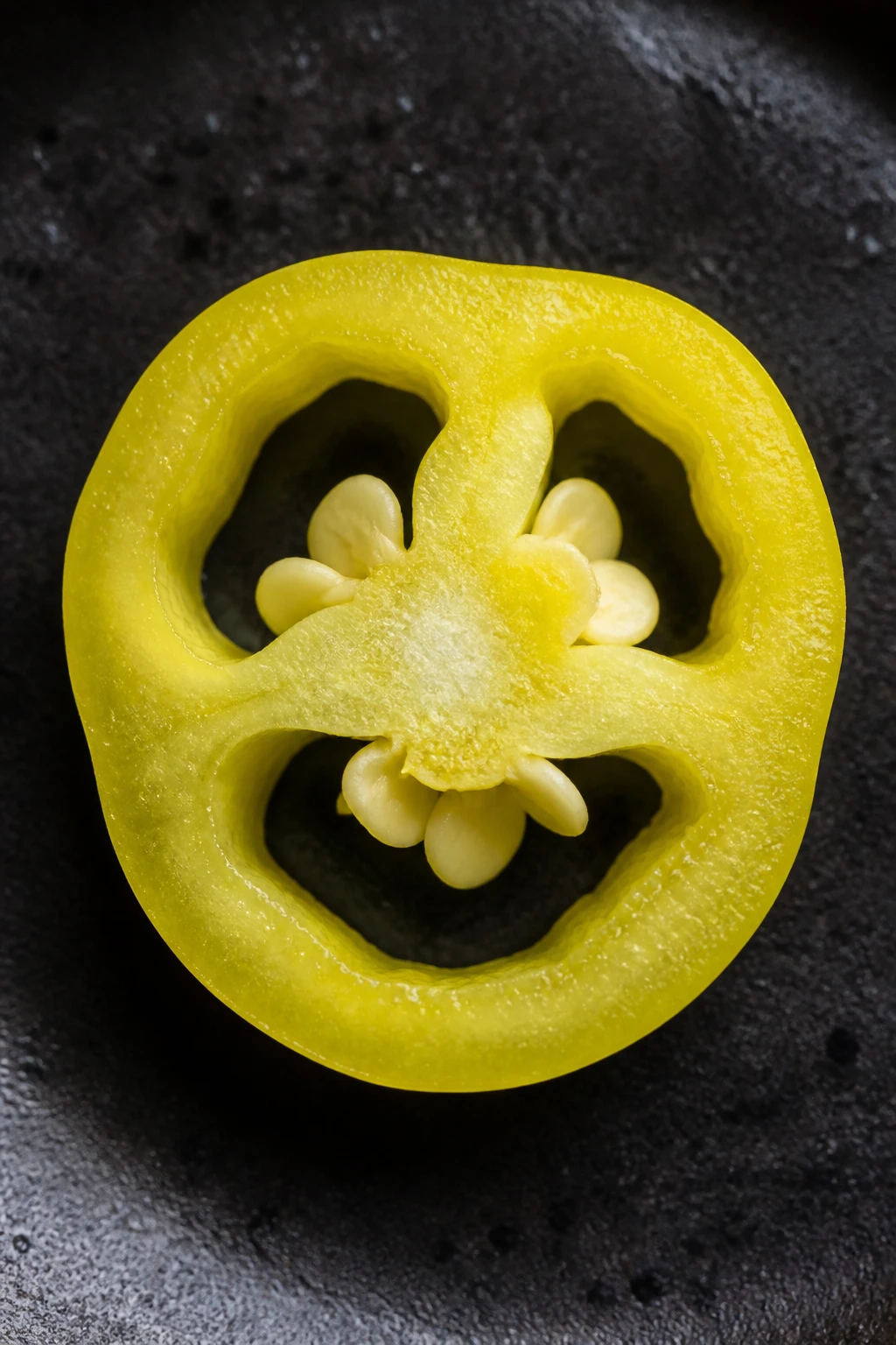 Macro shot of a single sliced banana pepper cross-section on dark plate