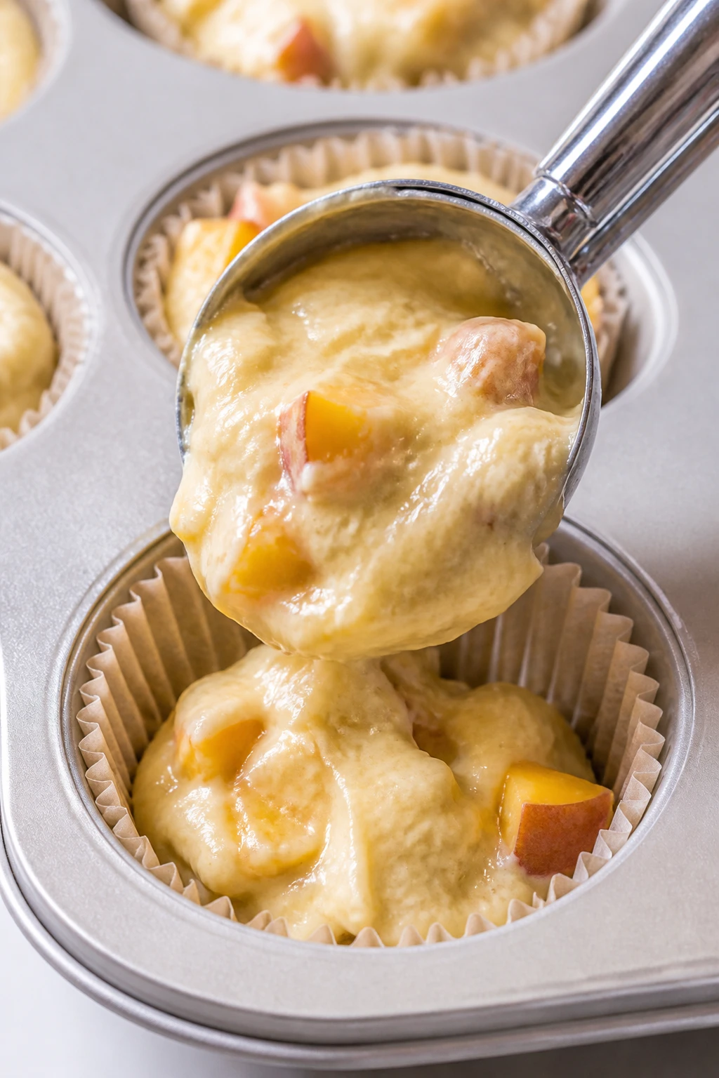 Closeup of vanilla peach muffin batter being scooped into liner, single dish