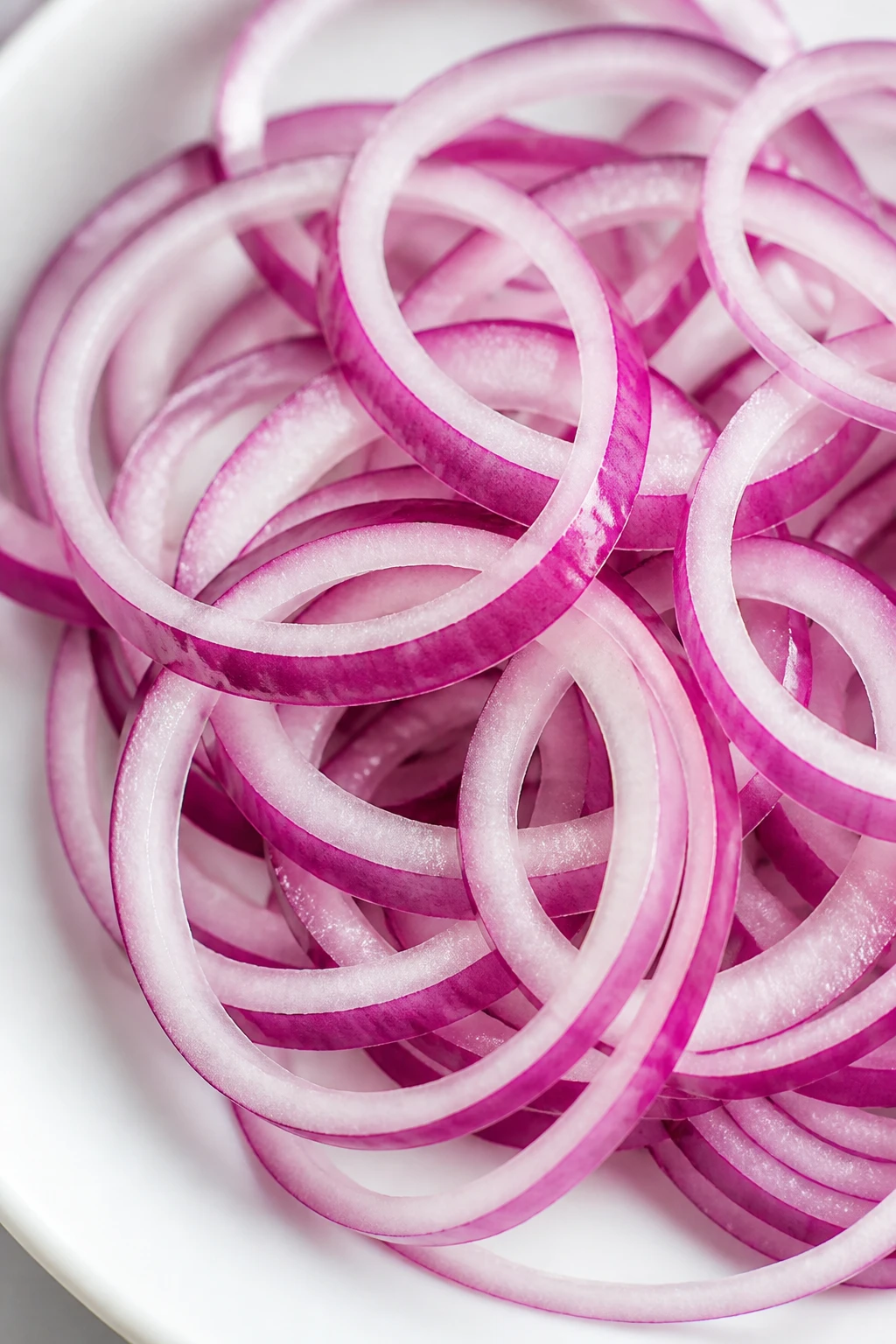 Closeup of thin red onion rings on a white plate, vivid layers
