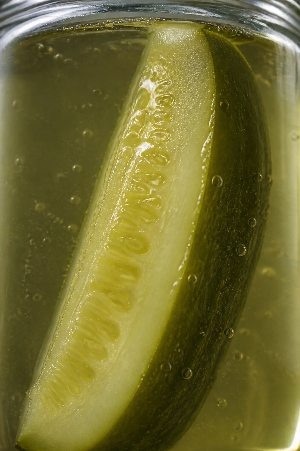 Closeup of a single cucumber spear submerged in brine jar