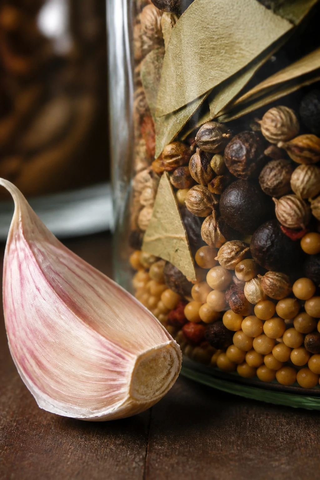 Closeup of garlic clove beside pickling spices in jar