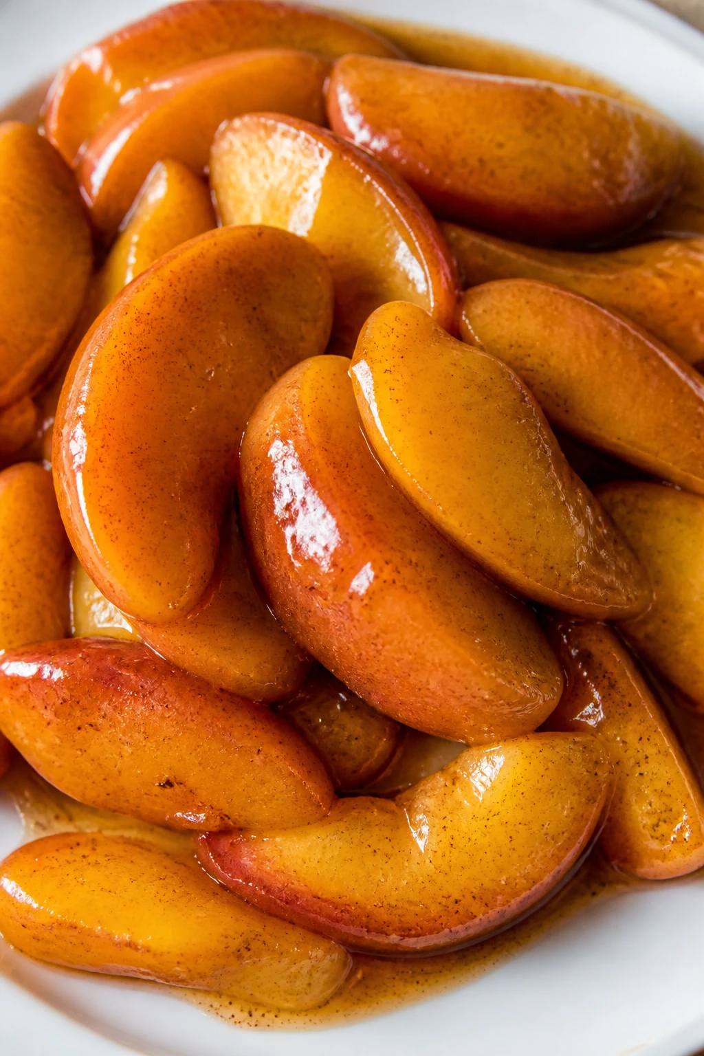 closeup sliced peaches with cinnamon-speckled glaze, white plate